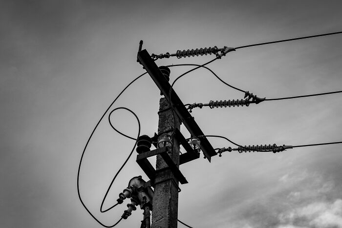 A black and white image of a power pole with wires and insulators against a cloudy sky, representing scary things people witness.