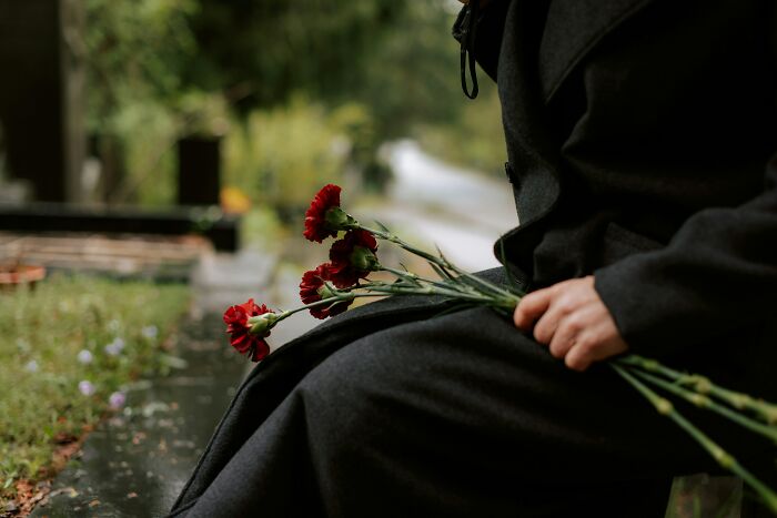 Scariest things witnessed: A person in a dark coat sits outdoors, holding red flowers, in a somber scene.