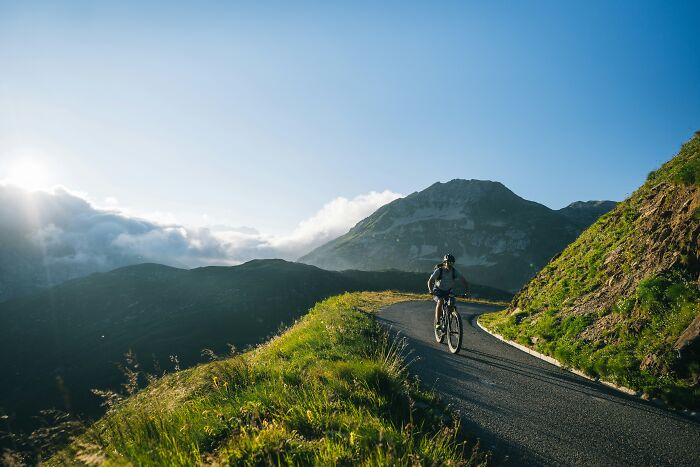 A person riding a bicycle on a winding mountain road, a scariest thing to witness, with a bright sun.