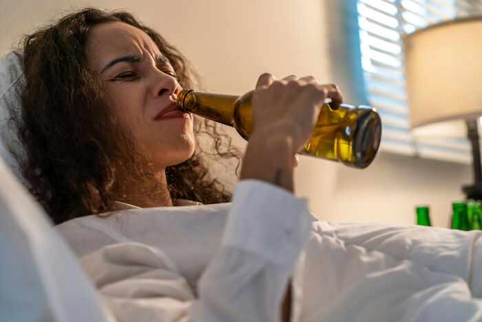 A woman grimacing while drinking from a beer bottle in bed, illustrating scariest things witnessed related to a*******n.