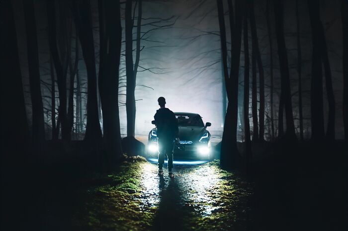 A person standing in a dark, misty forest, illuminated by a car's headlights, representing scariest things witnessed.
