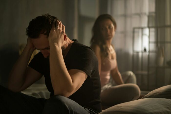 A man holding his head in frustration, with a woman sitting behind him. This image evokes scariest things people witness.