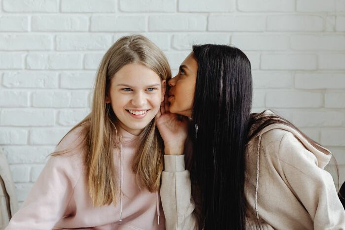 Two girls whispering and smiling, showcasing social dynamics related to gender roles.