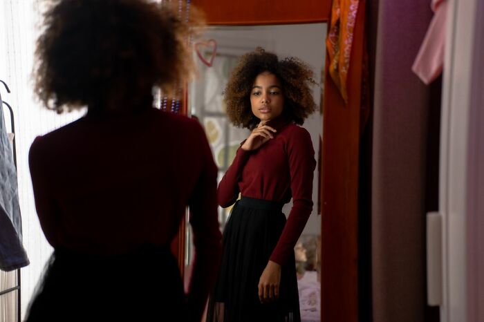 A young woman looking at her reflection in a mirror, contemplating societal gender roles and toxic femininity.