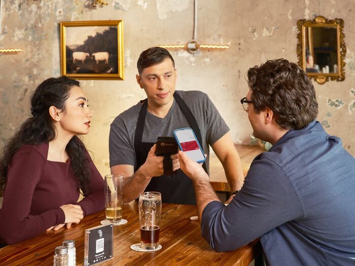A server is taking payment from a couple at a table, an example of gender roles and toxic femininity.
