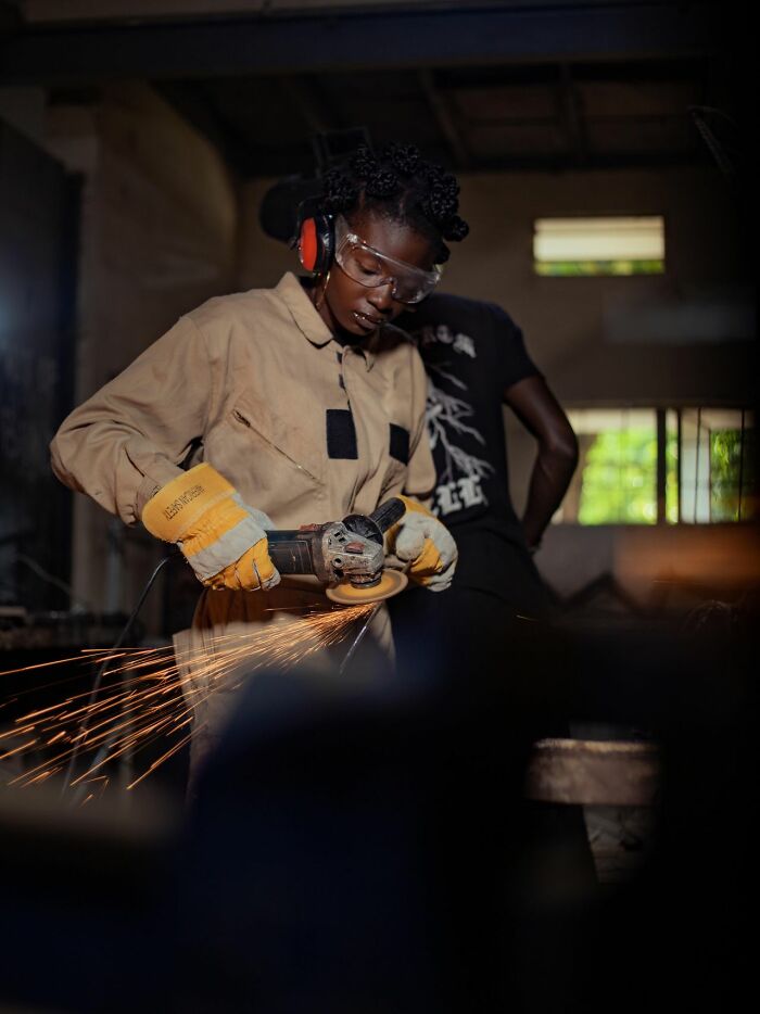 A woman wearing safety gear uses a power tool, challenging gender roles and toxic femininity.