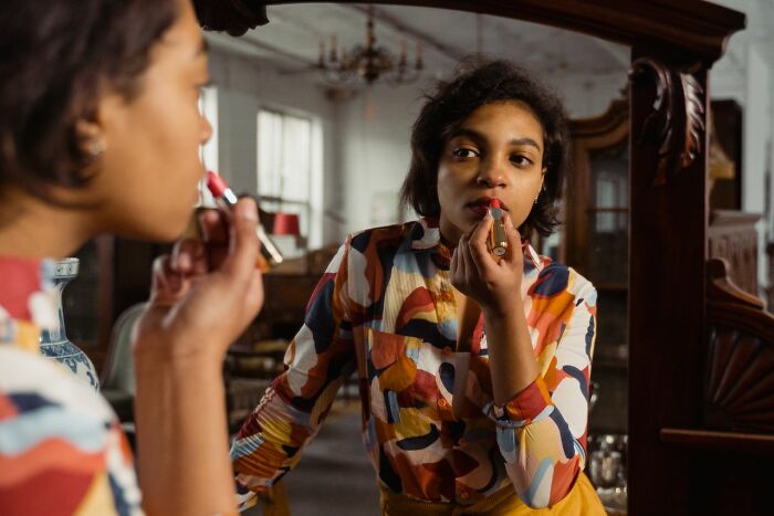 A woman applying red lipstick while looking into a mirror, representing an aspect of femininity.