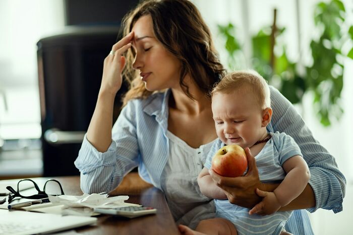 A stressed mother holding a crying baby, highlighting the pressures of gender roles and potential toxic femininity.