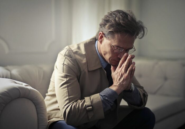 A man looking contemplative, with his hands clasped, reflecting on societal gender roles.