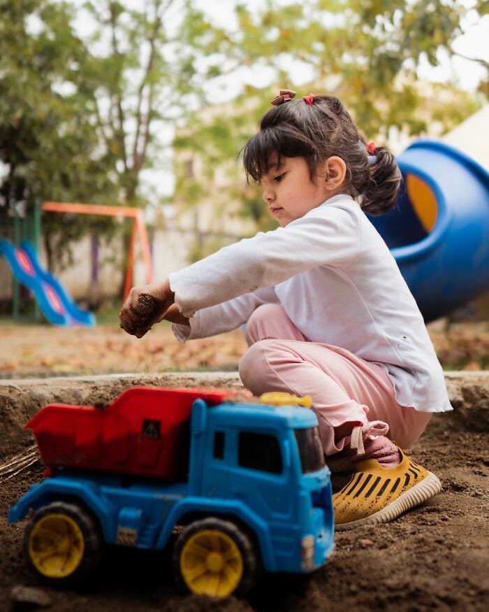 A young girl playing with a toy dump truck in the sand, defying traditional gender roles.