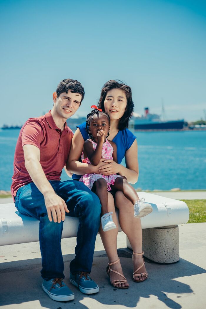 A multi-racial family of three sitting on a bench by the water, illustrating examples of toxic femininity.