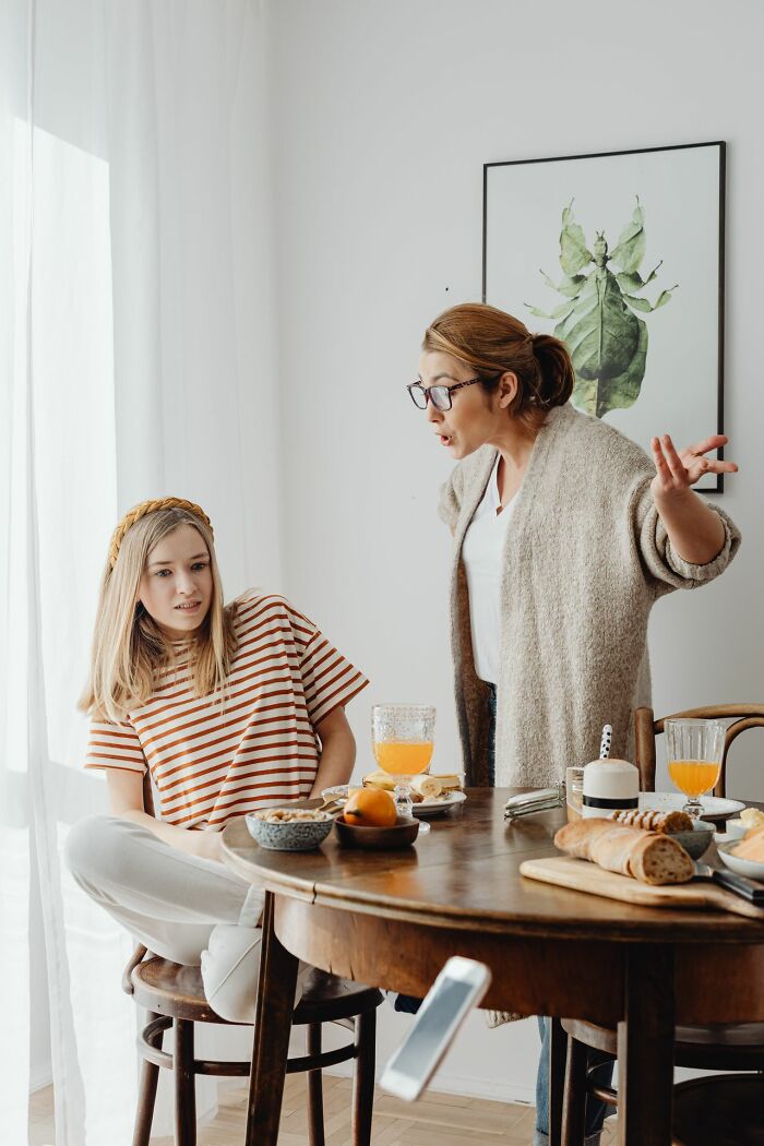 Woman gesturing angrily at a younger woman at a table, depicting a controversial example of toxic femininity.