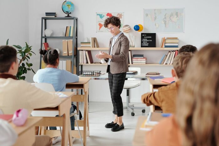 Teacher in a classroom full of students, illustrating a learning environment for understanding gender roles and toxic femininity.