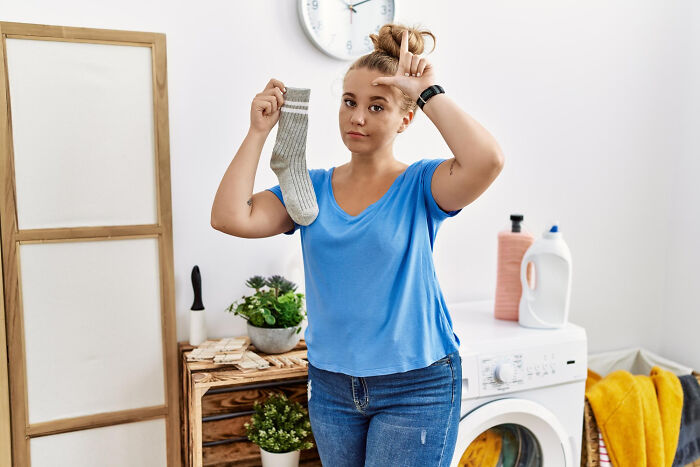 A woman holds a single sock and makes an L-sign on her forehead, indicating a loss in relationships and affairs.