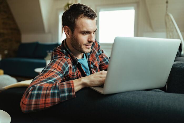 A man in a plaid shirt on a couch using a laptop, where affairs can come to light.