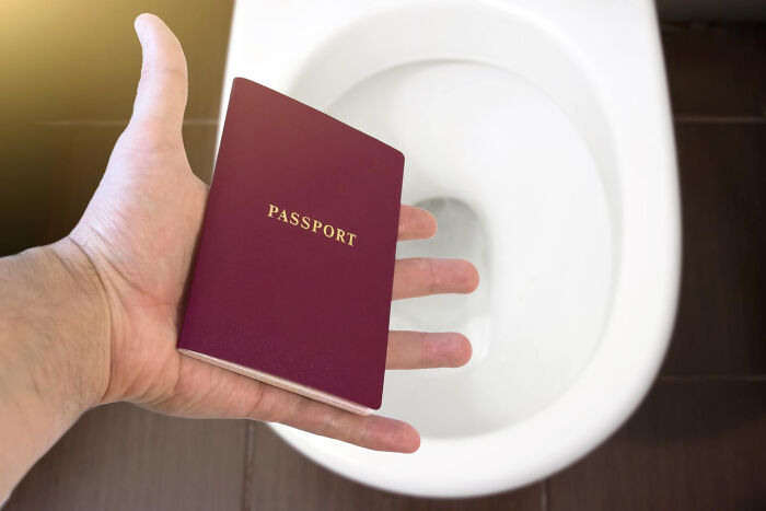 A hand holding a passport over a toilet, a brutal way affairs come to light.