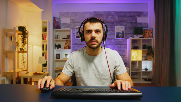 A man with headphones looks directly at the camera while gaming, perhaps unaware of affairs coming to light.
