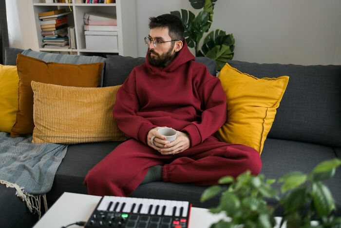 Man in red tracksuit on a couch, holding a mug. Affairs can come to light in brutal ways for partners.