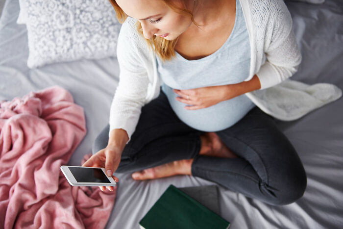 A pregnant woman on a bed looking at her phone, revealing affairs and secrets.