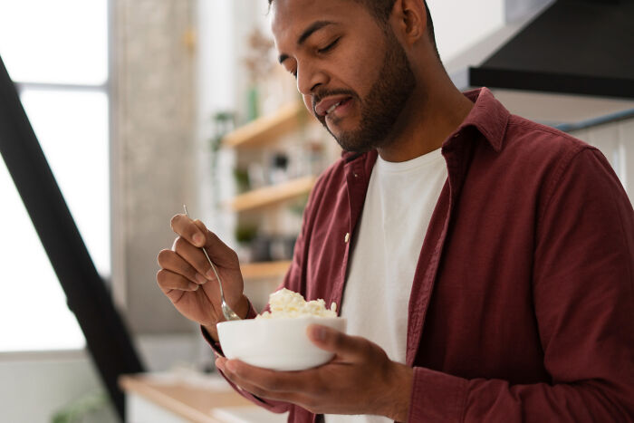 Man eating from a bowl, unaware of affairs coming to light in a brutal way for his partner.