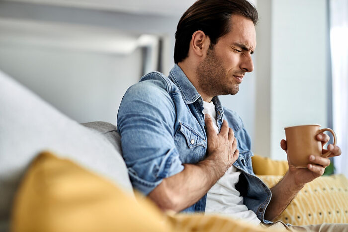 Man clutches chest in pain, holding a mug, as partner's affairs came to light brutally.