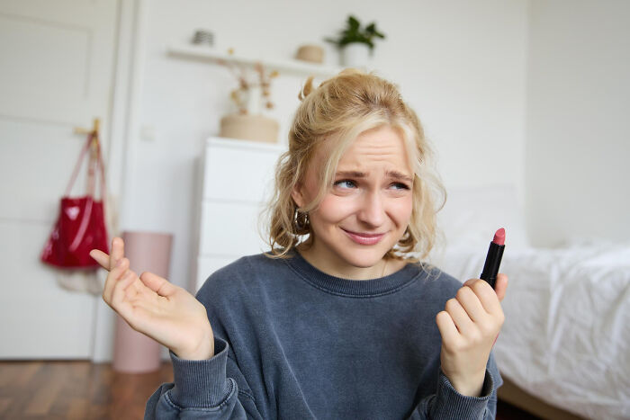Blonde woman looks confused, holding lipstick, wondering about affairs coming to light for partners.
