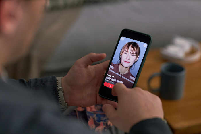 A person uses a dating app on their phone, swiping left on a profile, possibly revealing an affair.