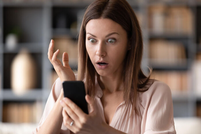 Shocked woman looking at her phone. Affairs can come to light in brutal ways for partners.