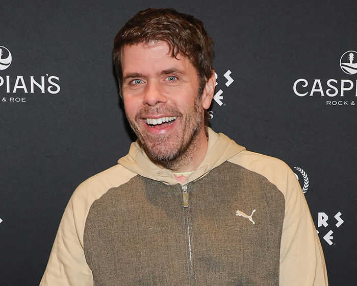 Perez Hilton smiling, revealing a heartbreaking question related to his hospital bed experience and family's secret answer.