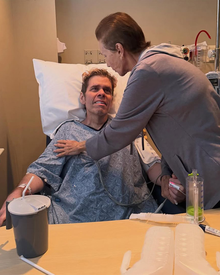 Perez Hilton in a hospital bed, looking up at someone leaning over him, as he faces a heartbreaking question.