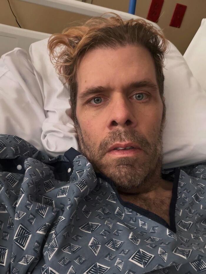 Perez Hilton in a hospital bed, looking directly at the camera with a somber expression, revealing his crisis. Perez Hilton in a hospital bed, looking directly at the camera with a somber expression, revealing his crisis.