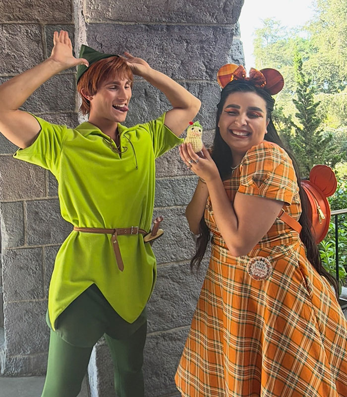 A smiling woman in a plaid dress with Minnie Mouse ears next to a man dressed as Peter Pan.