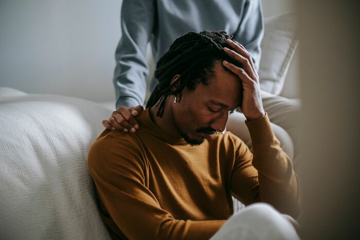 A man holding his head in distress while someone places a comforting hand on his shoulder, symbolizing relationship red flags and mental health.