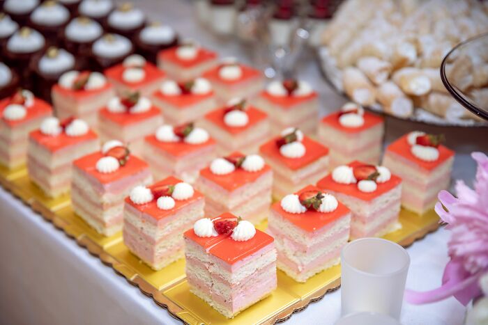 A table full of delicate pastries with pink frosting and strawberry garnishes, ready for an office celebration, or to read work drama stories.