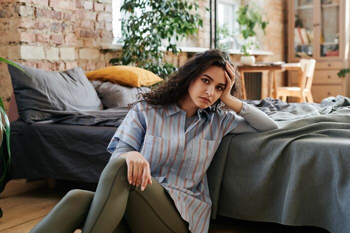 A woman sitting on the floor by her bed, looking distressed, conveying a moment she realized they’re with the very wrong person.