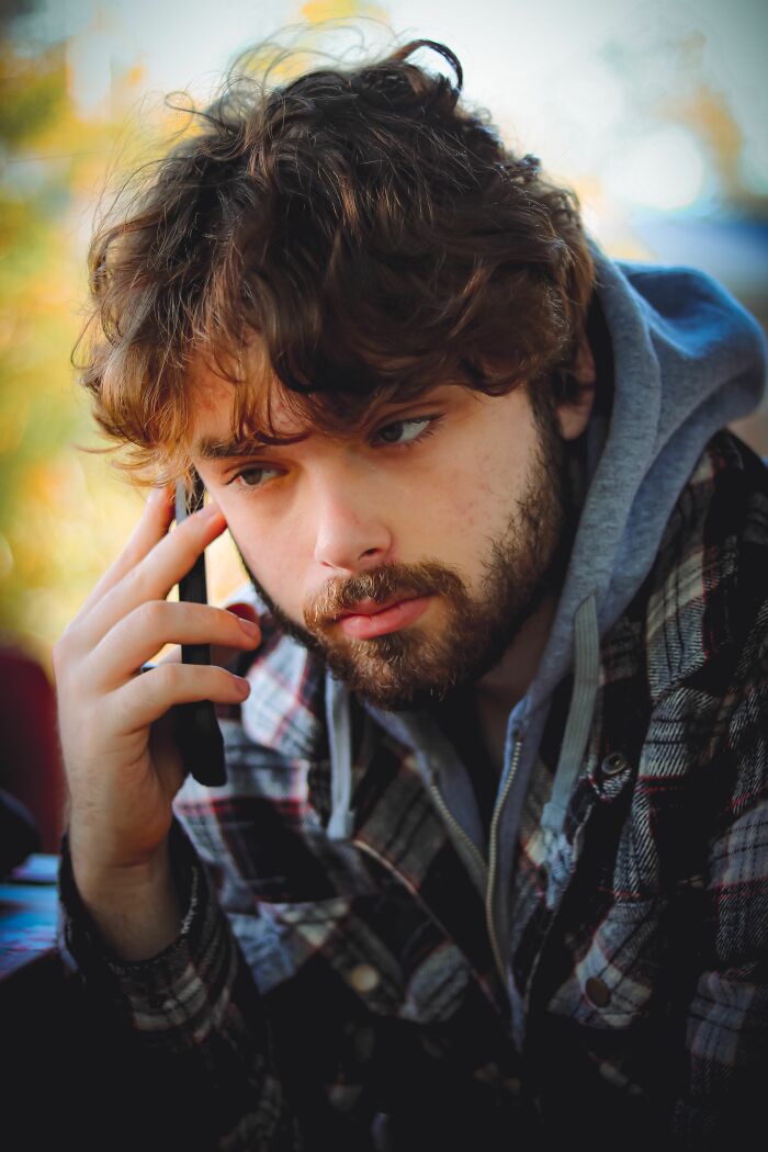 A man with a beard and curly hair looks concerned while talking on a phone, realizing he's with the wrong person.