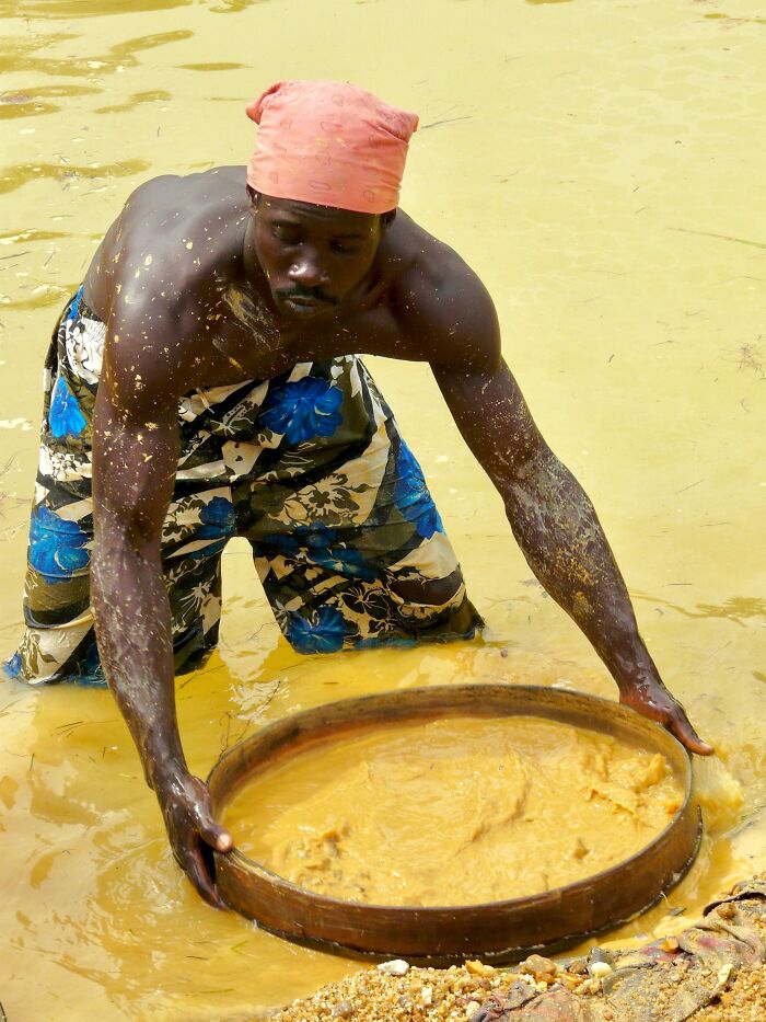 A man in traditional clothing panning for gold in muddy water, related to misconceptions about wealth.