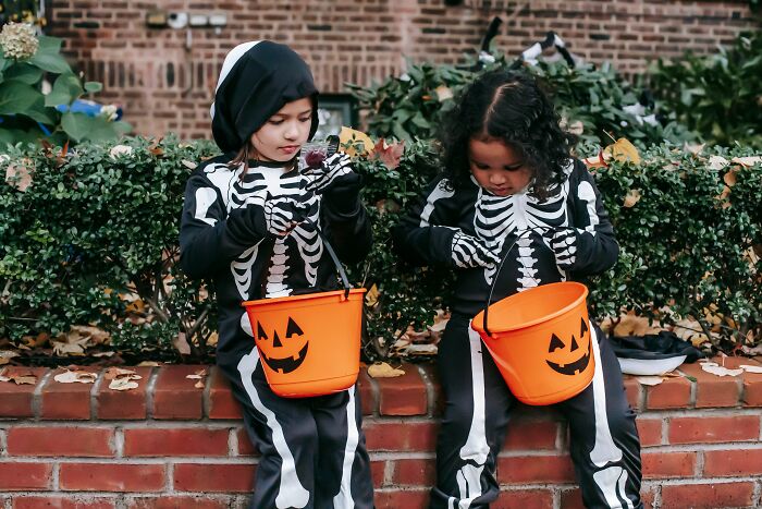Two children in skeleton costumes with pumpkin buckets for Halloween, a unique aspect of America.