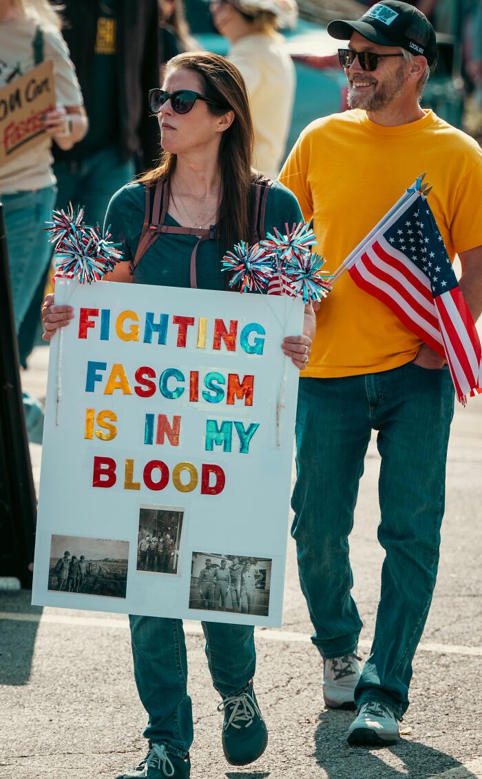 A woman holding a sign saying "Fighting Fascism is in my Blood" with a man holding an American flag. People believe today that propaganda influences beliefs.