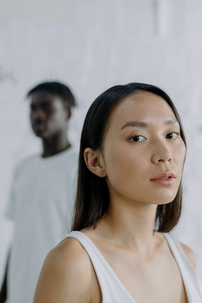 A woman looking at the camera, with a man blurred in the background, signaling they are the very wrong person for each other.