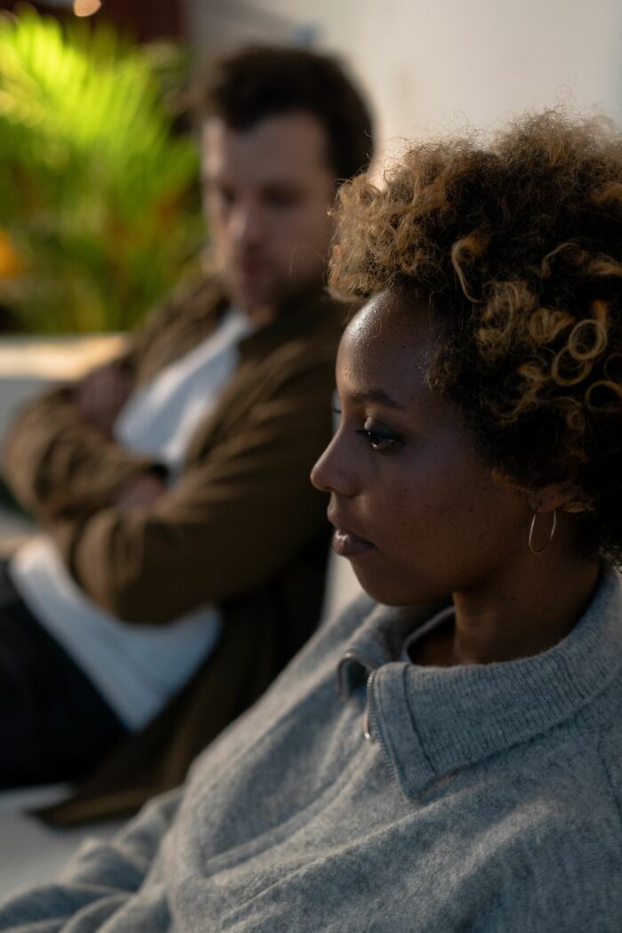 A woman with curly hair looks away from a man with crossed arms in the background, illustrating the exact moment a boyfriend said something.