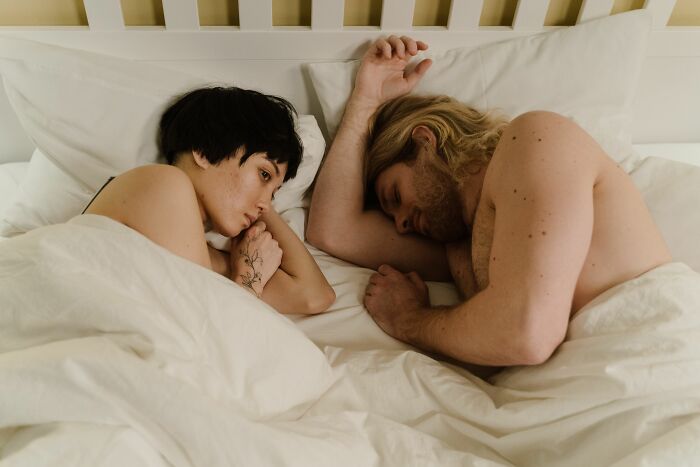 A woman is awake next to a sleeping man in bed, pondering if she's with the wrong person.