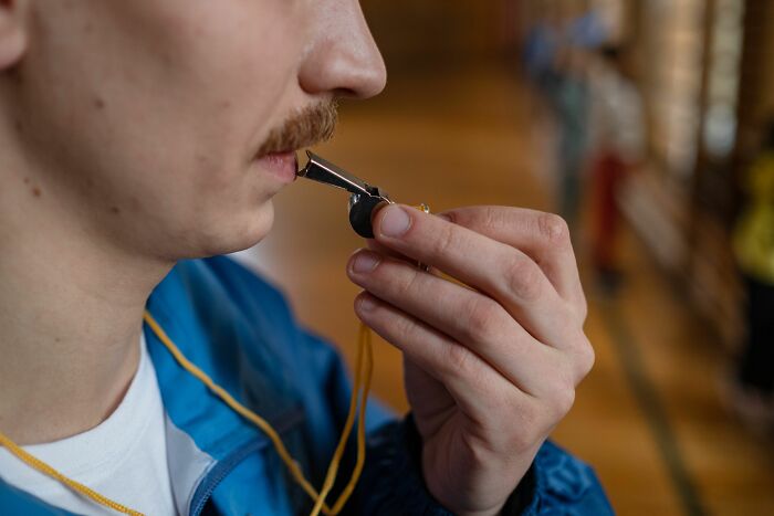 Close-up of a person with a mustache blowing a whistle, picking up skills in 30 days.
