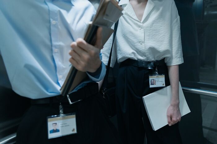 Two coworkers with ID badges, carrying files, potentially discussing personal details or PTSD.