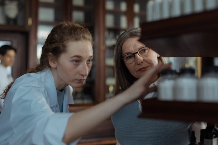 Two women, possibly medical field workers, looking at bottles on a shelf, demonstrating their work.