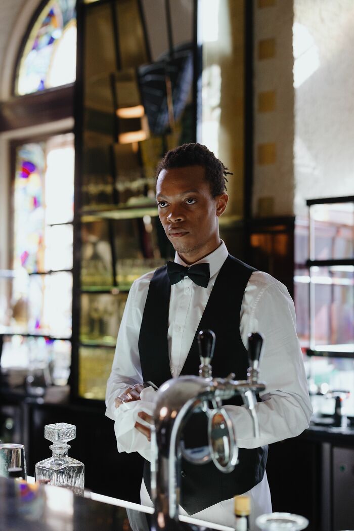 A bartender in a vest and bow tie, reflecting on personal details or experiences related to PTSD.