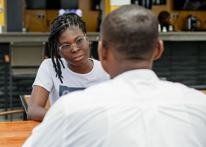 A young woman with glasses intently listens to a man across from her, capturing the exact moment a boyfriend said something.