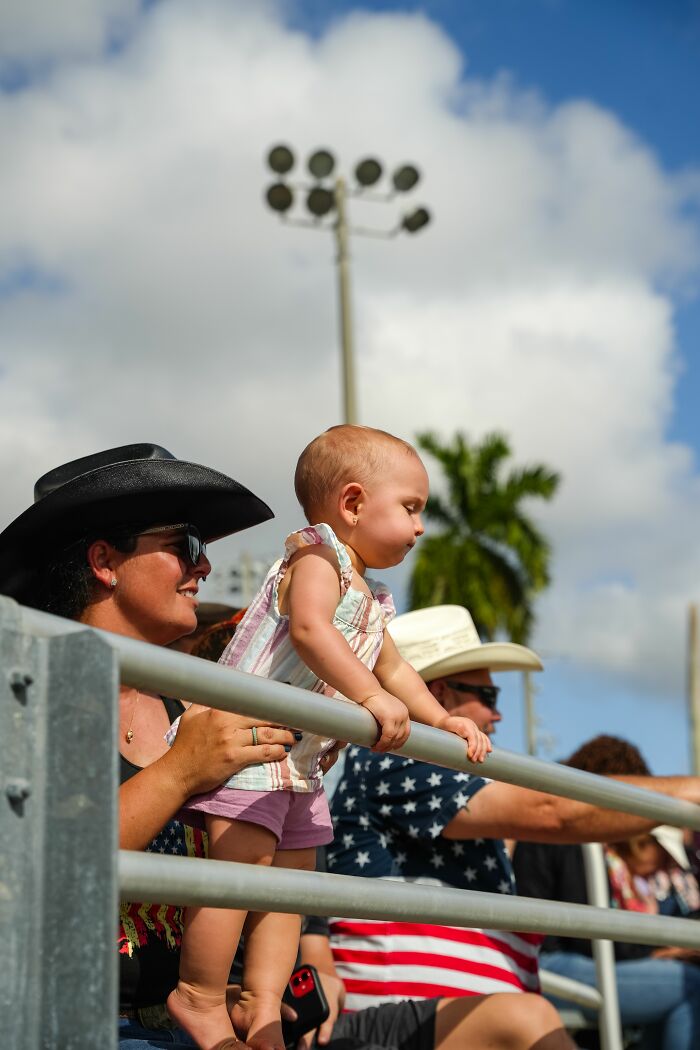 A baby and adults in cowboy hats watching an event, showing things about America.