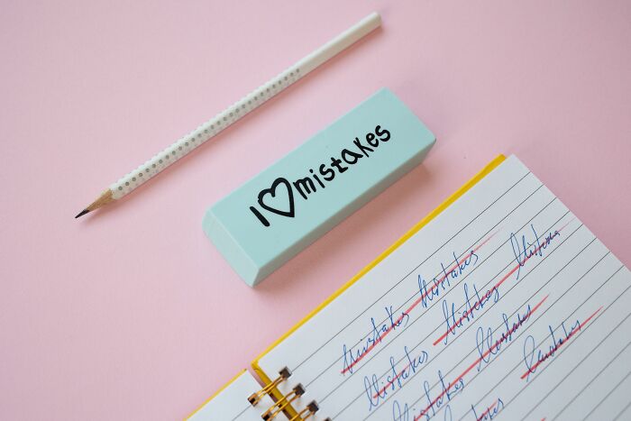 A pencil, an eraser with I Love Mistakes, and a notebook with many misspelled words crossed out in red. A pencil, an eraser with I Love Mistakes, and a notebook with many misspelled words crossed out in red.