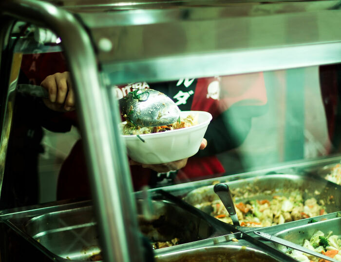 A close-up of a person serving a kid's school lunch from a buffet line, comparing school lunch in France to USA. A close-up of a person serving a kid's school lunch from a buffet line, comparing school lunch in France to USA.